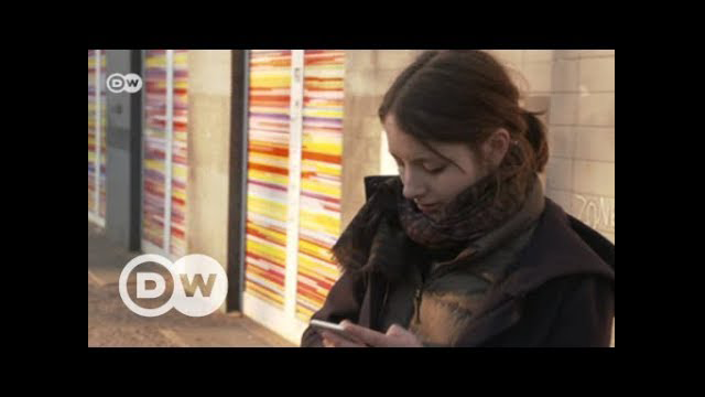 Janina Mütze steht vor einem Haus und schaut auf ihr Mobiltelefon