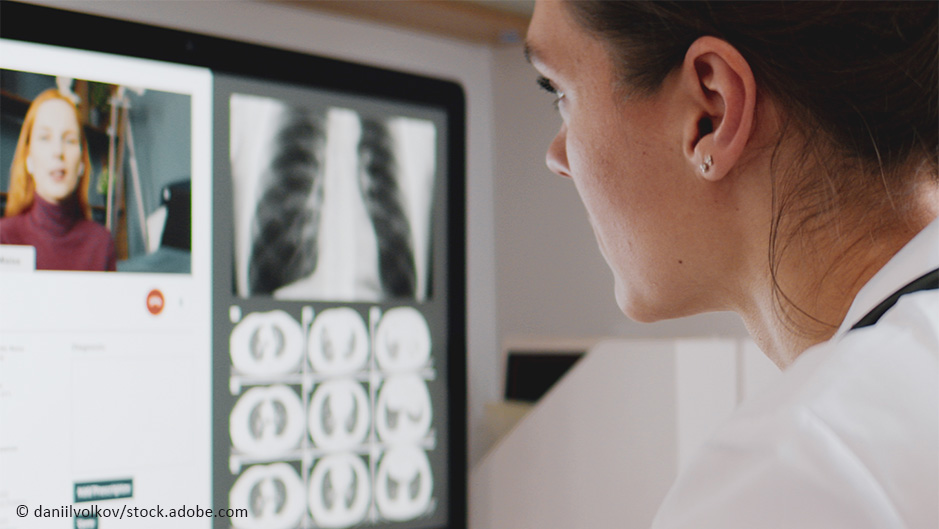Ärztin sitzt vor einem Computer. Sie spricht online mit einer Patientin über deren Röntgenaufnahmen, die auf dem Computer zu sehen sind.